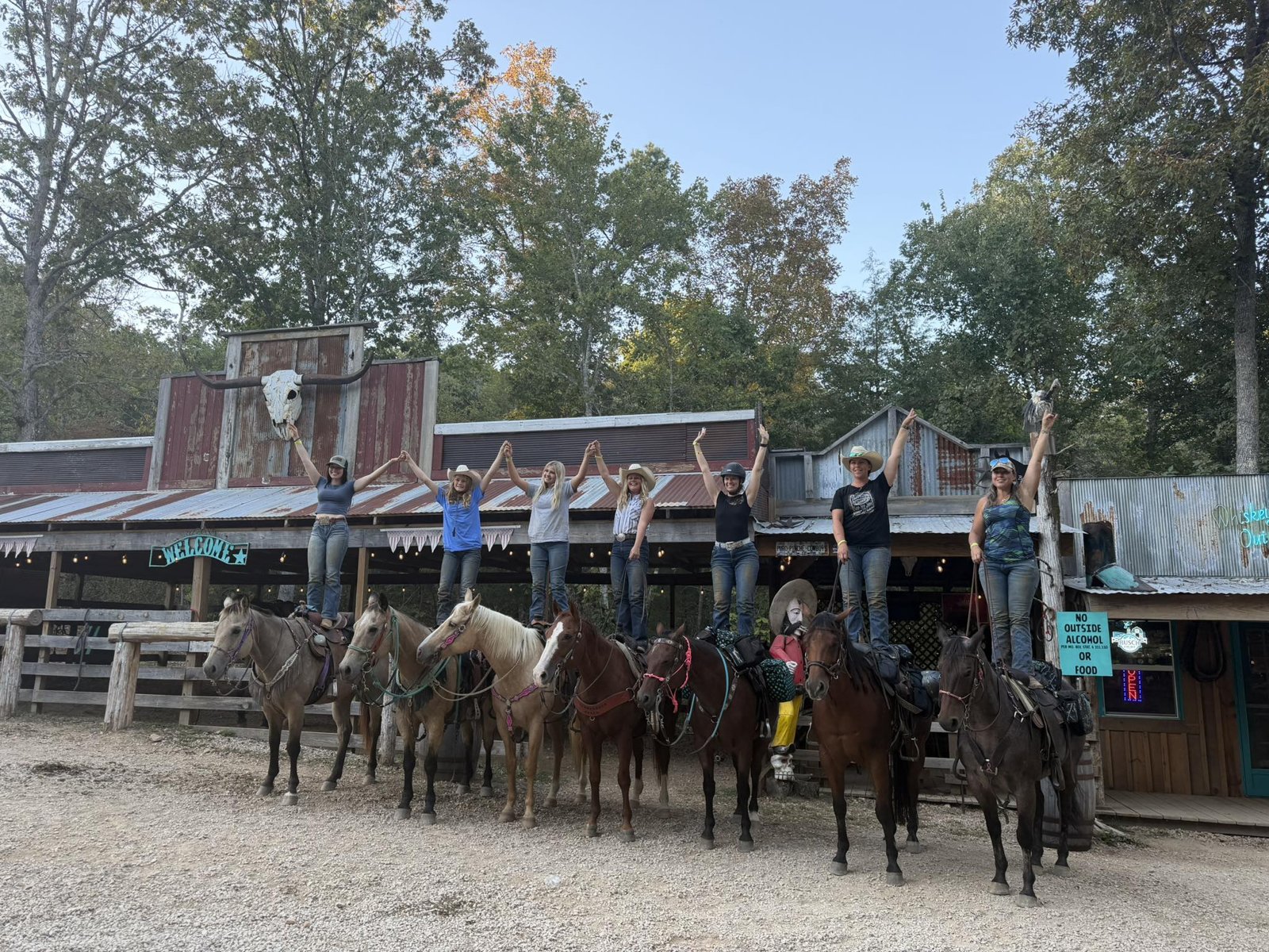 Riders standing on their saddles in front of Whiskey River Outpost
